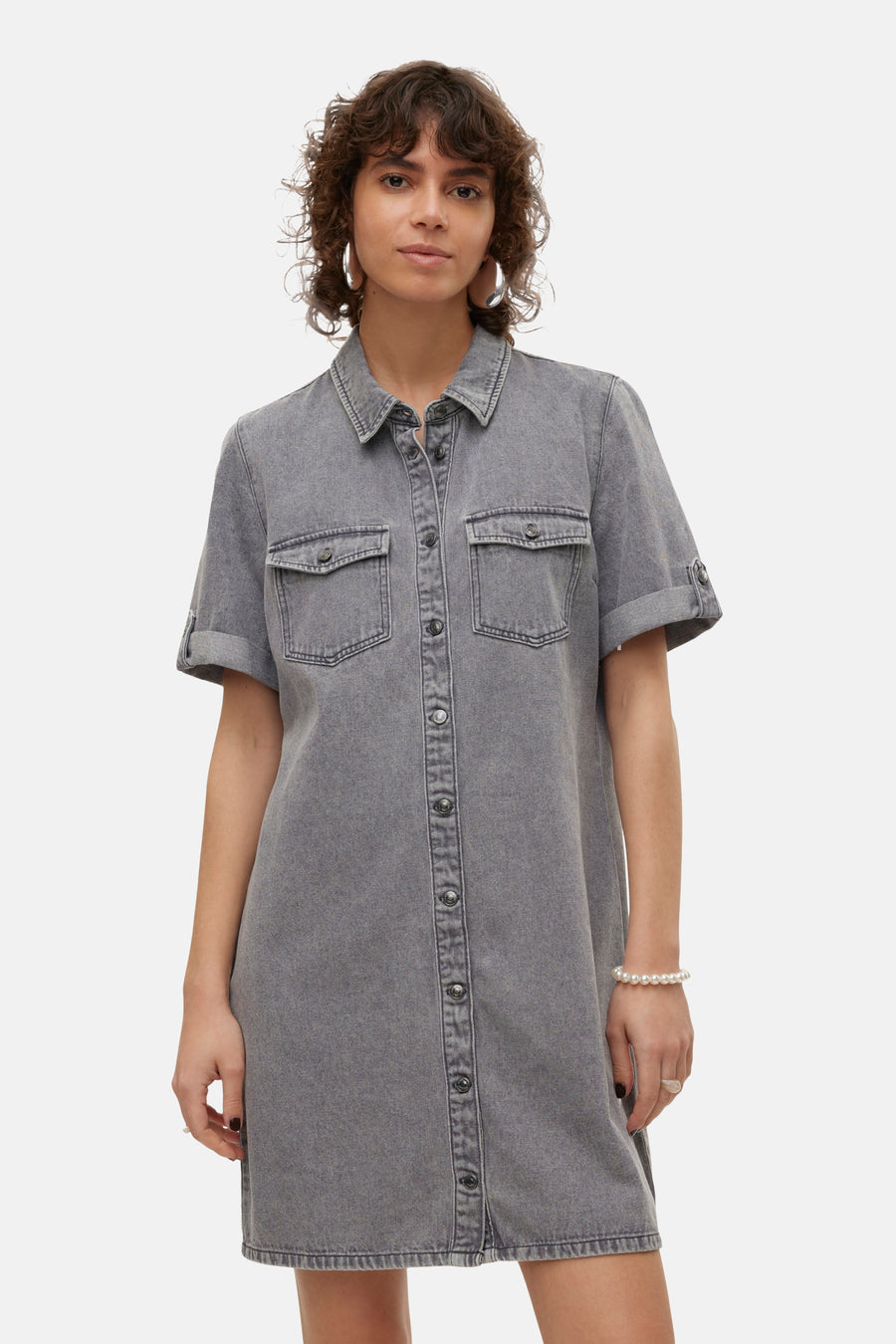 Grijs kleedje met korte mouwen van VERO MODA, met knoopsluiting en borstzakken, gecombineerd met een parelarmband en grote zilveren oorbellen.
