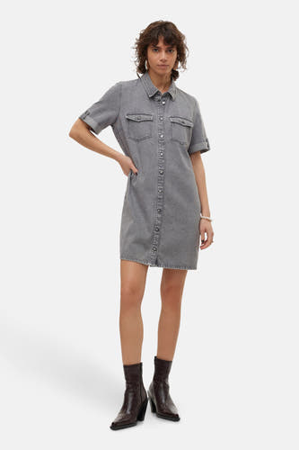 Vrouw in grijze denim jurk met knopen en bruine laarzen.