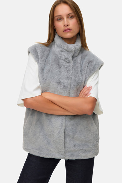 Gilet gris de VERO MODA, avec une texture fausse fourrure, porté sur une chemise blanche et un pantalon foncé.