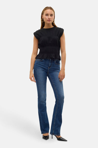 Donkerblauwe flared jeans van VERO MODA, gecombineerd met een zwarte top en zwarte pumps.