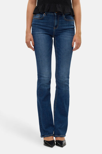 Donkerblauwe flared jeans van VERO MODA, met een klassieke denim textuur en zwarte schoenen.
