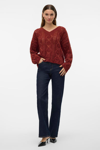 Bruine V-hals pull van VERO MODA®, met ajour gebreid patroon en lange mouwen, gedragen met donkere jeans en zwarte hakken.
