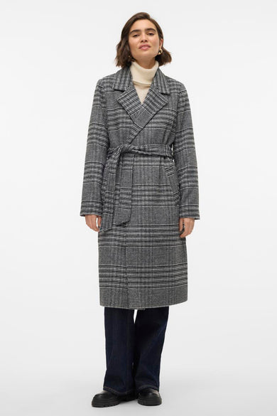 Grijze lange jas van VERO MODA met ruitpatroon en strikceintuur, gedragen over een crèmekleurige coltrui en donkere jeans.
