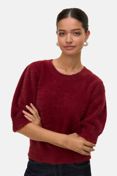 Rode trui met ronde hals van VERO MODA®, zachte textuur, met gekruiste armen poserende vrouw draagt zilverkleurige oorbellen.
