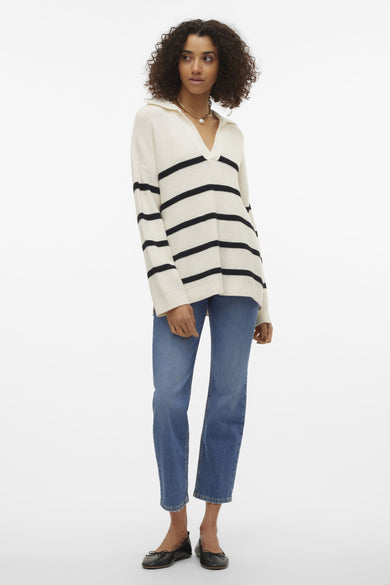 Pull-over blanc à col V de VERO MODA, rayé de noir, associé à des jeans et des ballerines noires.