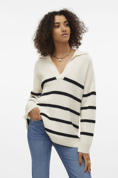 T-shirt à col V blanc de VERO MODA® avec des rayures noires, porté avec un jeans et une chaîne en or.