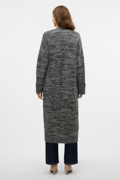 Zwart gilet van Vero Moda, gezien van achteren, met een lange snit over een donkere jeans en beige hakken.
