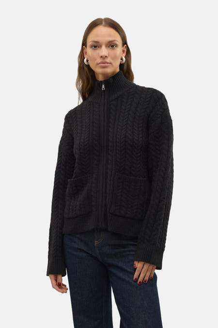 Zwart gilet van Vero Moda met kabelpatroon, lange mouwen, twee zakken en gedragen met een donkere jeans.
