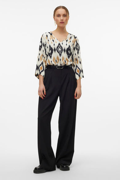 Multikleurige blouse van VERO MODA met ikat-patroon, driekwart mouwen en een zwarte broek met riem.

