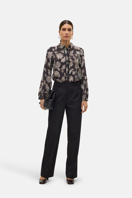 Zwarte broek van VERO MODA®, met wijde pijpen en een gladde textuur, gecombineerd met een geprinte blouse en clutch.
