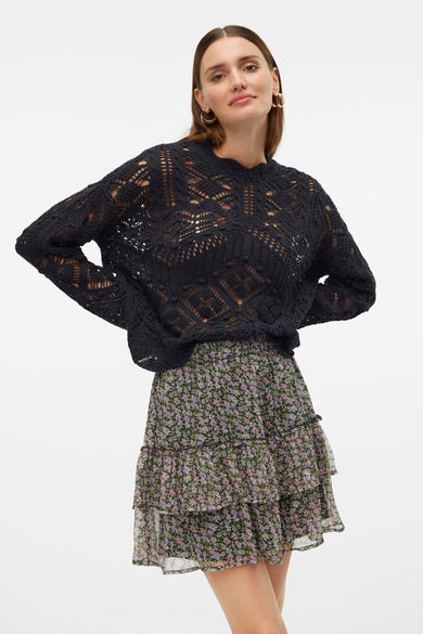 Pull noir avec col rond de VERO MODA, avec un décolleté ouvert et porté avec une jupe imprimée.