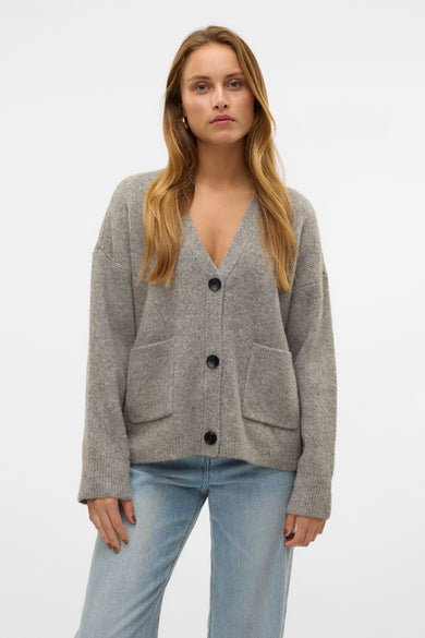 Grijs vest van Vero Moda met lange mouwen, knoopsluiting en zakken, gedragen over een spijkerbroek.
