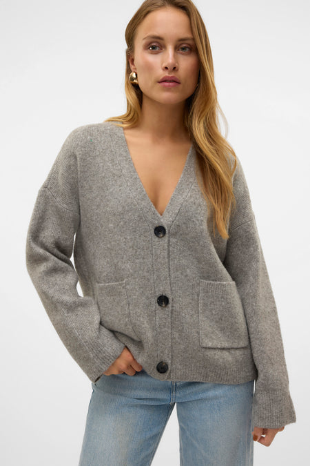 Grijs vest van VERO MODA, met lange mouwen, knoopsluiting en opgestikte zakken, gedragen over een blauwe spijkerbroek.
