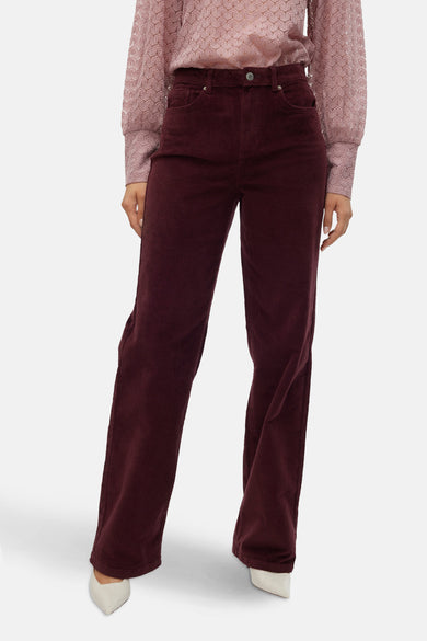 Bordeaux broek van VERO MODA, met wijde pijpen en gemaakt van corduroy, gecombineerd met een roze blouse met bloemenpatroon.
