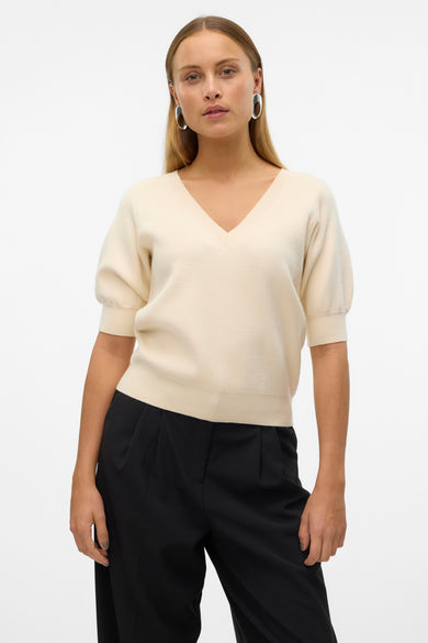 Ecru trui met V-hals van Vero Moda, gecombineerd met een zwarte pantalon en zilverkleurige oorringen.