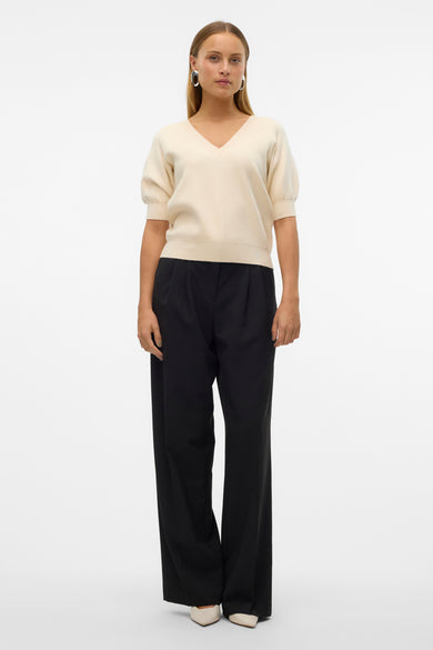 Ecru pull met V-hals van VERO MODA®, gecombineerd met een zwarte pantalon en crèmekleurige schoenen.
