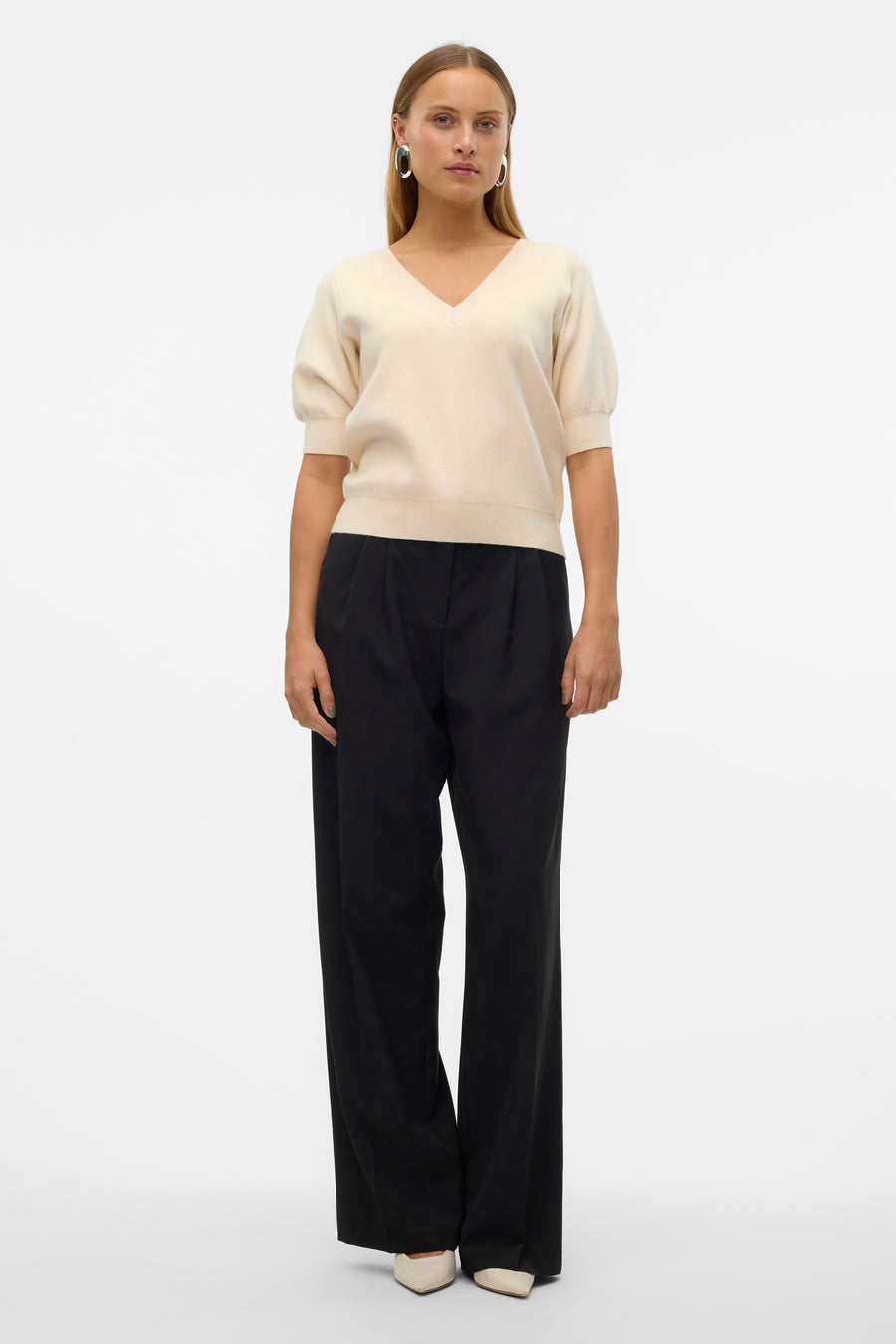 Pull écru à col V de VERO MODA®, associé à un pantalon noir et des chaussures crème.