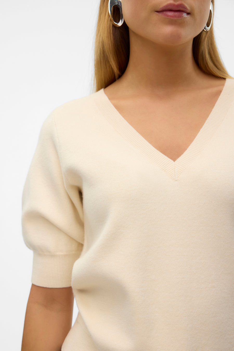 Pull écru avec col V de VERO MODA, avec manches courtes et boucles d'oreilles argentées.