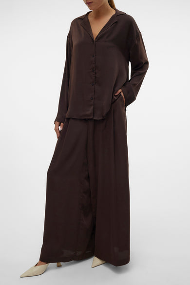 Bruine broek van VERO MODA, wijd uitlopend met een satijnen afwerking en gecombineerd met een bruin satijnen overhemd.