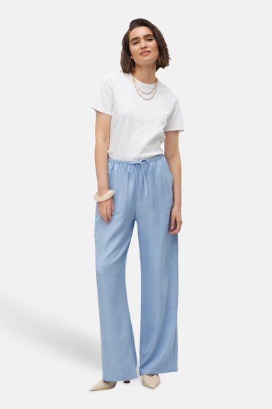 Blauwe kleurbroek van VERO MODA, gecombineerd met een wit T-shirt, gouden ketting en beige schoenen.
