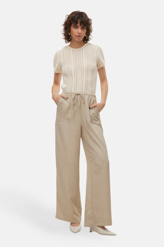 Jean beige de VERO MODA®, avec des jambes larges et des poches, porté avec un haut écru tricoté et des chaussures pointues.