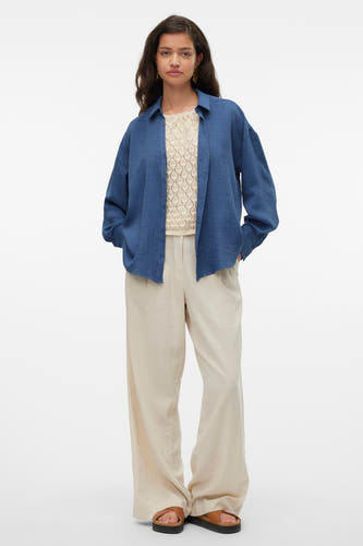 Blauw hemd met lange mouwen van VERO MODA®, gedragen over een gebreide top met een open structuur en lichte, wijde broek.
