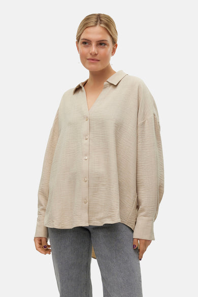 Chemise beige à manches longues de VERO MODA®, avec fermeture boutonnée, portée avec un jean gris et des chaussures marron.