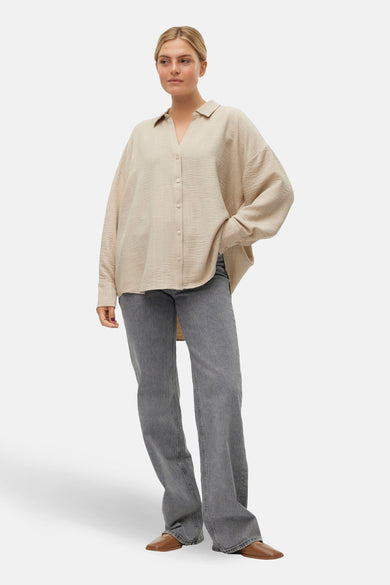 Beige hemd met lange mouwen van VERO MODA®, met knoopsluiting, gedragen met grijze jeans en bruine schoenen.