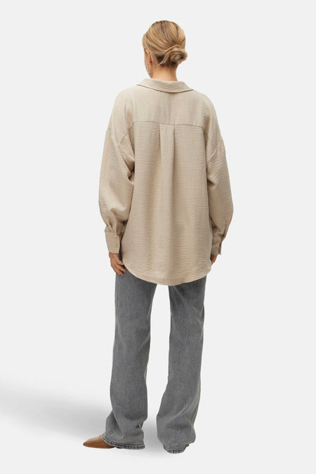 Beige overhemd met lange mouwen van VERO MODA, achterkant gezien, met lange broek en bruine schoenen.
