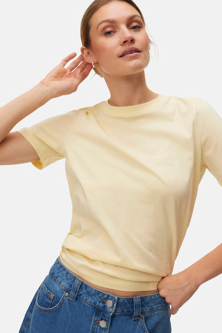 T-shirt jaune à manches courtes de VERO MODA®, porté avec une jupe en jean bleue boutonnée et des chaussures assorties.