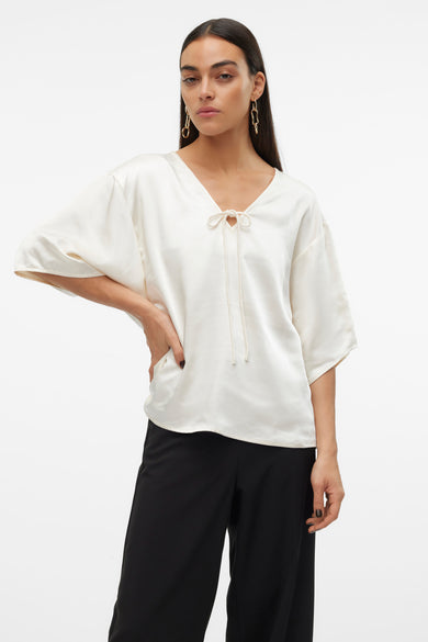 Ecru blouse met driekwart mouwen van VERO MODA, met een v-hals en koorddetails, gecombineerd met een zwarte broek.