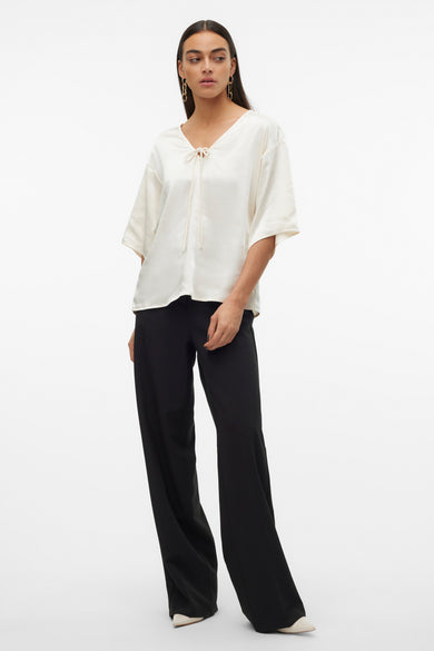 Ecru blouse met driekwart mouwen van VERO MODA, met een knoopdetail en gedragen met zwarte, wijde pijpen en hakken.
