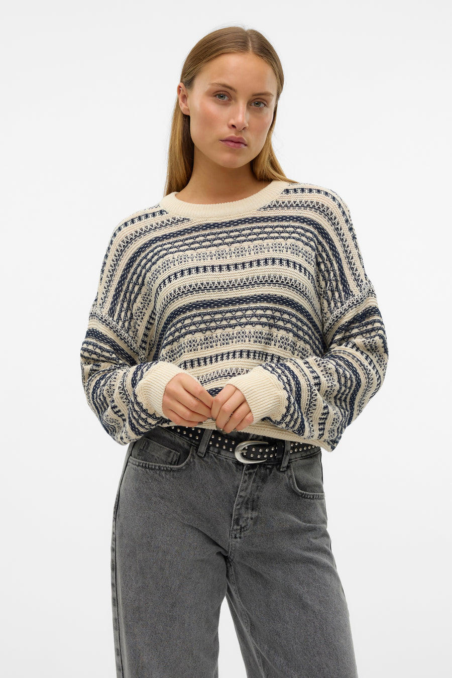 Ecru trui met ronde hals van VERO MODA, met donkerblauwe strepen en grijze jeans met riem.
