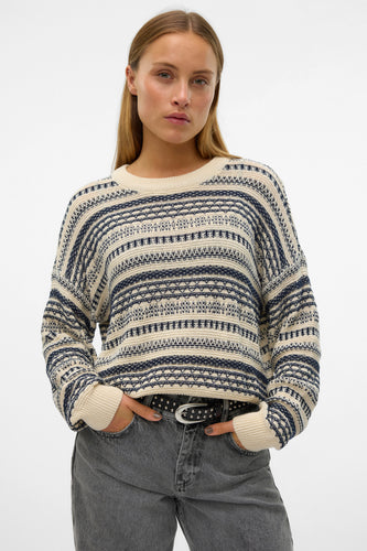 Ecru trui met ronde hals van Vero Moda, met blauwe strepen en een geometrisch patroon, gedragen met grijze jeans en een riem met studs.

