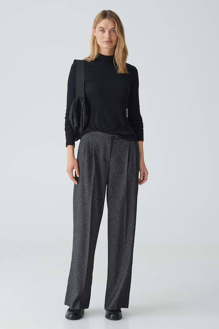 Zwarte trui met ronde hals van OPUS, lange mouwen en gedragen met een grijze pantalon en zwarte tas.

