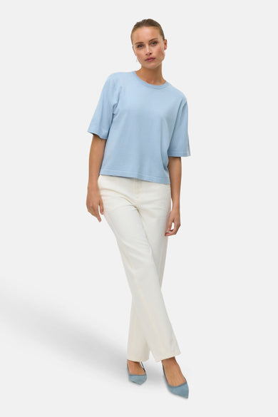 Blauwe trui met ronde hals van VERO MODA, gedragen met een witte broek en blauwe schoenen.
