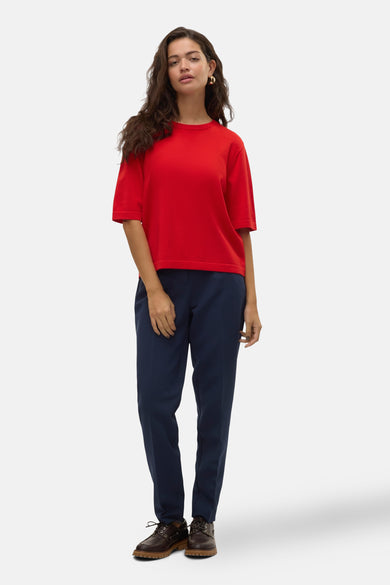 Rode trui met ronde hals van VERO MODA®, gedragen met een donkerblauwe pantalon en bruine schoenen.
