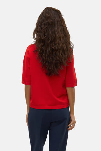 Pull rouge à col rond de VERO MODA®, dos, combiné avec un pantalon bleu foncé et des cheveux bouclés lâches.