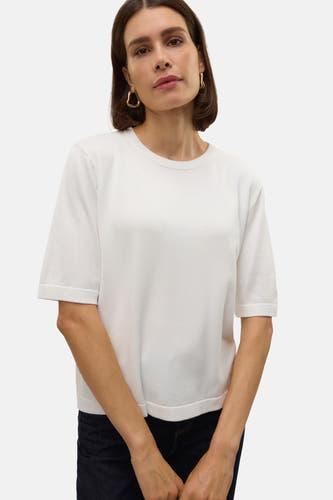Witte trui met ronde hals van VERO MODA, met korte mouwen, gedragen met donkere jeans en gouden oorbellen.
