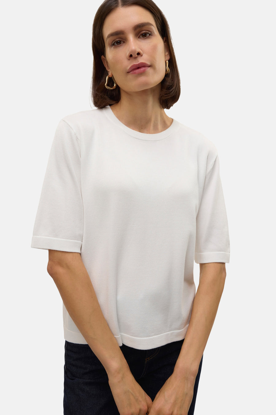 Witte trui met ronde hals van VERO MODA, met korte mouwen, gedragen met donkere jeans en gouden oorbellen.