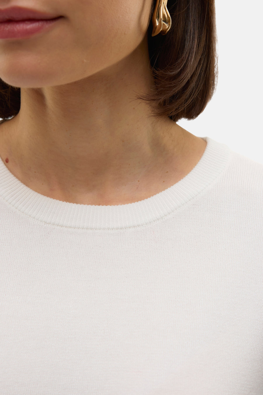 Witte trui met ronde hals van VERO MODA, detailopname met gouden oorbellen en donkerbruin haar.