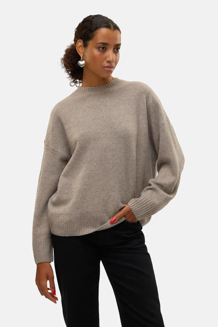 Bruine trui met ronde hals van VERO MODA, met lange mouwen, gecombineerd met een zwarte broek en zilveren oorbellen.
