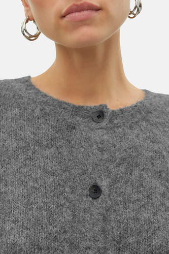 Grijze cardigan van VERO MODA, met knoopsluiting en een gebreide textuur, gedragen met zilverkleurige oorringen.

