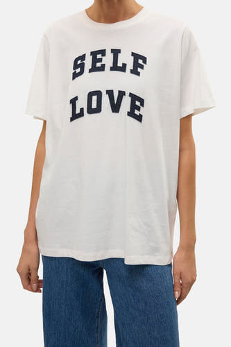 Wit T-shirt met korte mouwen van VERO MODA, met marineblauwe tekst "SELF LOVE", gecombineerd met een blauwe jeans.