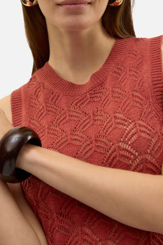 Bruine kleedje zonder mouwen van Vero Moda, met opengewerkt breipatroon, gedragen met gouden oorbellen en een donkerbruine armband.

