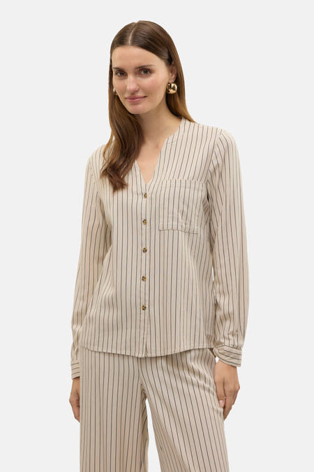 Chemise beige à manches longues de VERO MODA®, avec des rayures et une poche poitrine, portéeéeée pantalon rayé et des chaussures noires.