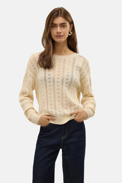 Ecru trui met ronde hals van VERO MODA, met een opengewerkt breipatroon, gedragen met een donkere spijkerbroek en gouden oorbellen.
