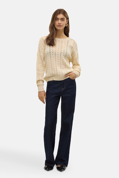 Ecrukleurige trui met ronde hals van Vero Moda, met ajourpatroon, gecombineerd met donkere jeans en zwarte schoenen.
