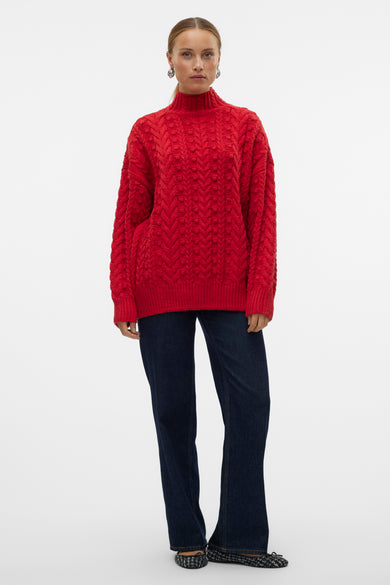 Pull rouge à col rond de VERO MODA, avec un motif côtelé et porté avec des jeans foncés et des chaussures plates.