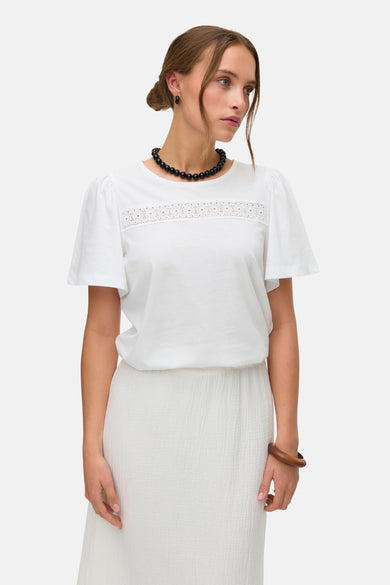 Blouse blanche à manches courtes de Vero Moda, avec des détails sur les bords et associée à une longue jupe crème.